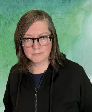 headshot of Jen wearing glasses and black hoodie in front of a green background.