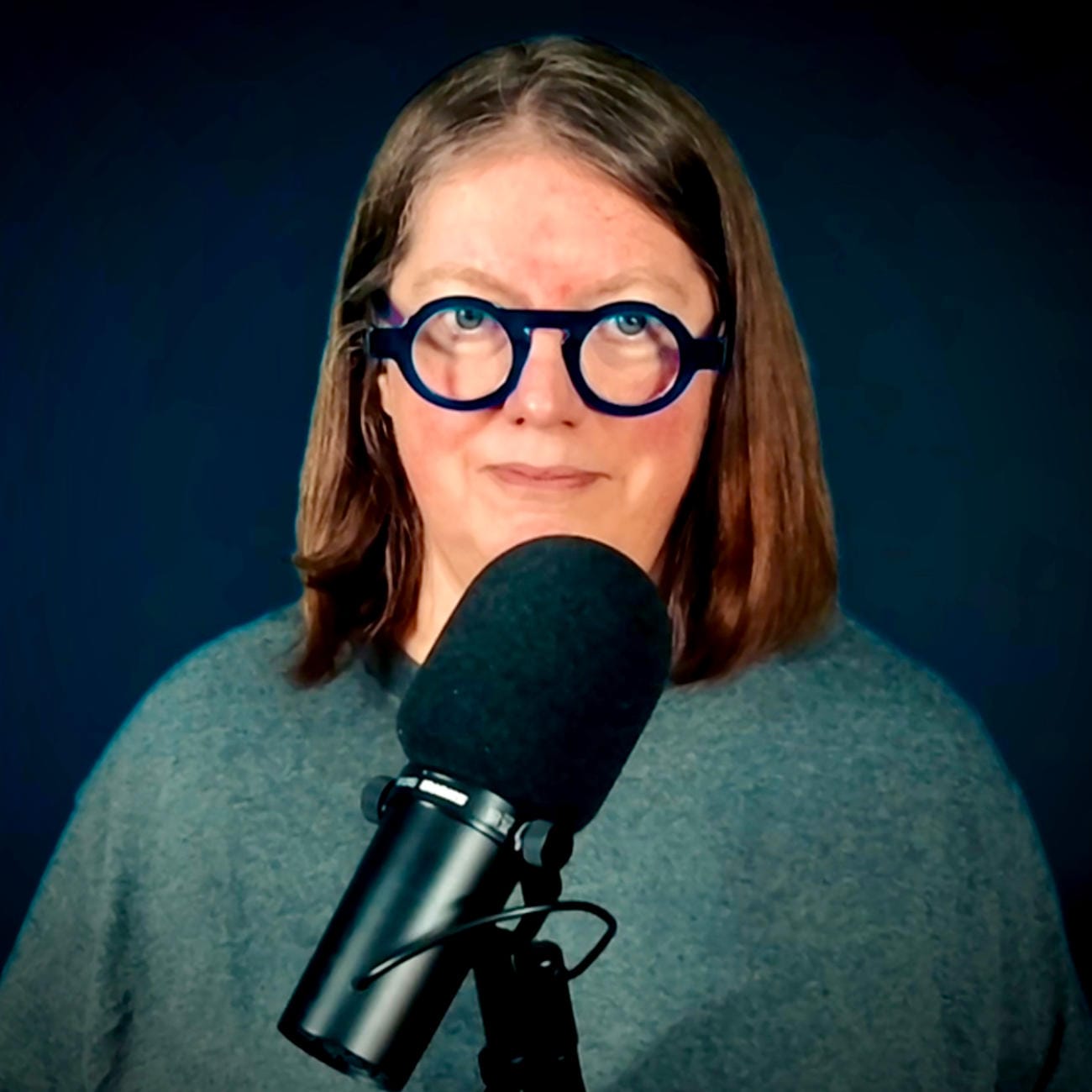 headshot of Jen wearing glasses and black hoodie in front of a green background.